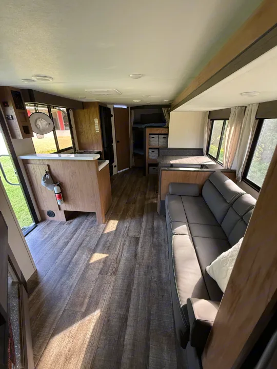 Spacious RV rental interior with wood-look flooring. Features a living area, kitchen, dinette, and bunk beds.. Forest River Campsite Reserve 2025
