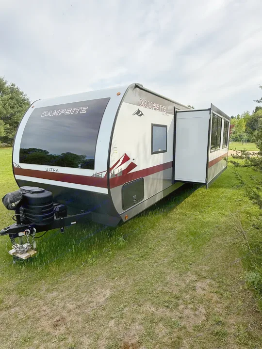 A Campsite Ultra travel trailer, ideal for RV rental, is parked on green grass under a cloudy sky.. Forest River Campsite Reserve 2025