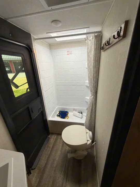Compact RV rental bathroom with shower (containing floaties), toilet, and black entry door.. Forest River Campsite Reserve 2025