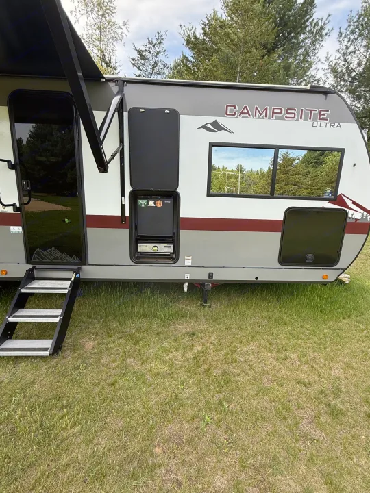 This RV rental is parked at a campsite, showcasing its extended awning, entry steps, and outdoor kitchen. Perfect for camping!. Forest River Campsite Reserve 2025