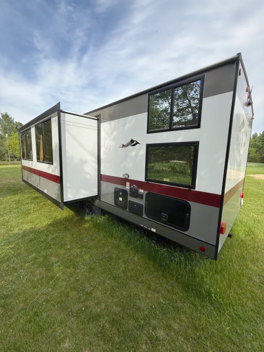 Modern rv rental travel trailer with extended slide-out, parked on green grass under a partly cloudy sky.. Forest River Campsite Reserve 2025