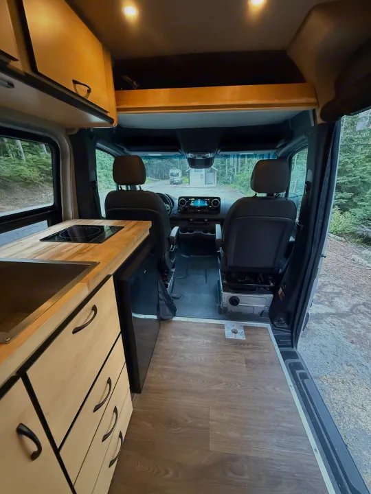 RV rental camper van interior, featuring a modern kitchenette (sink, cooktop, fridge), wood cabinets, and driver's area.. Mercedes-Benz Sprinter 2020