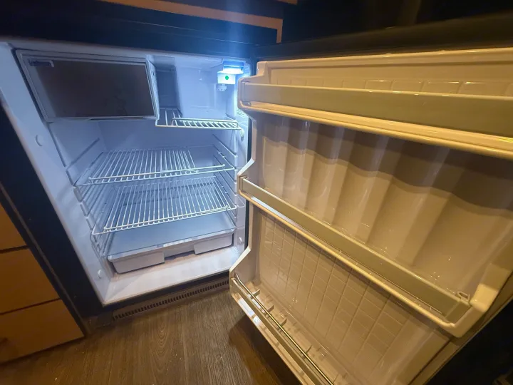 Inside a clean, empty RV rental refrigerator, open and ready for use. Features shelves, a freezer, and interior lighting.. Mercedes-Benz Sprinter 2020