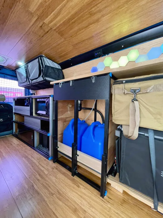 Explore this RV rental's organized camper van interior, featuring a functional kitchen area, water system, storage, and ambient LED lights.. Ford E350 2010