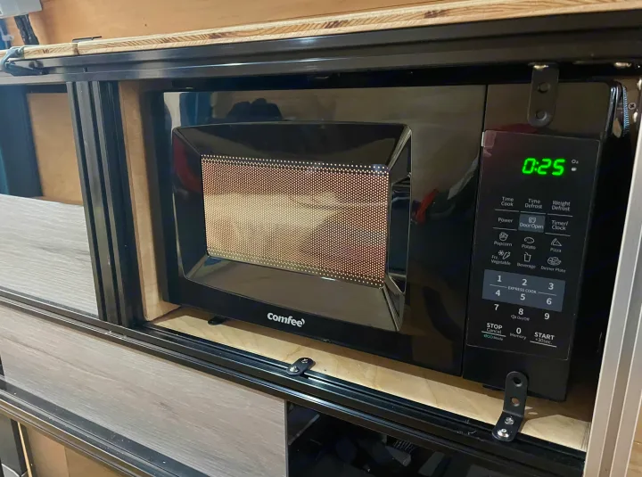 This black microwave oven, showing "0:25", is custom-installed in an RV rental, perfect for quick meals on the go.. Ford E350 2010