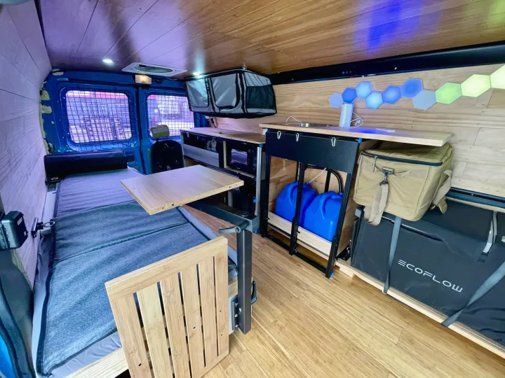 Cozy rv rental interior: A camper van with a bed, pull-out table, kitchenette, and ambient hexagonal lighting.. Ford E350 2010