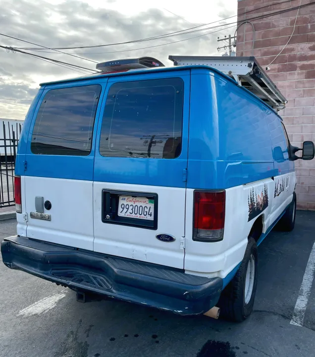 RV rental: Rear view of a custom blue and white Ford Econoline camper van with a roof rack, solar panels, and nature decals.. Ford E350 2010