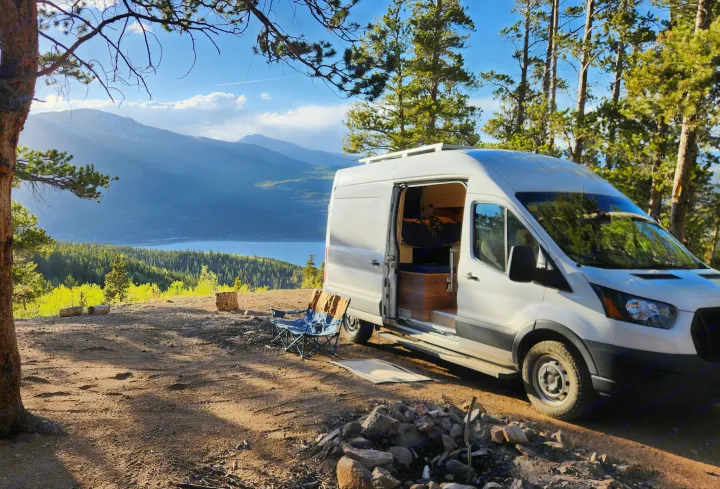 RV rental adventure: White camper van parked on a scenic mountain overlook with a lake view. Chairs and fire pit ready.. Ford Transit 2022