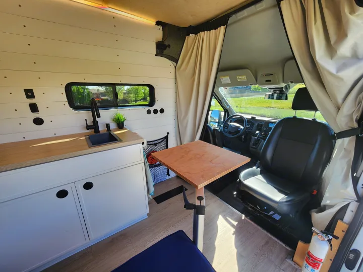 Modern rv rental interior with kitchenette, adjustable table, driver's seat, and privacy curtain. Ideal for comfortable travel.. Ford Transit 2022