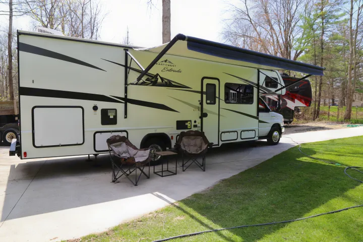 An East to West Entrada rv rental (Class C motorhome) with awning extended. Camping chairs and a small table are set up.. East to West Entrada 2023