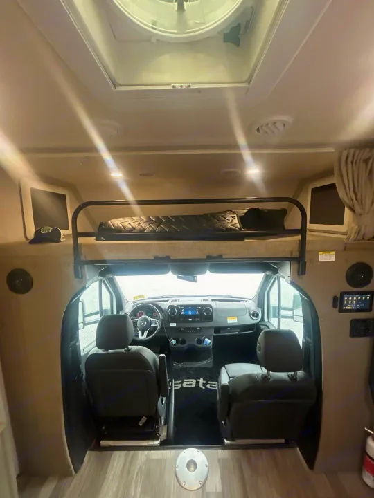 Modern RV rental interior: view from living area into the driver's cockpit, featuring an over-cab bunk and ceiling vent.. Isata 3 Series 2026