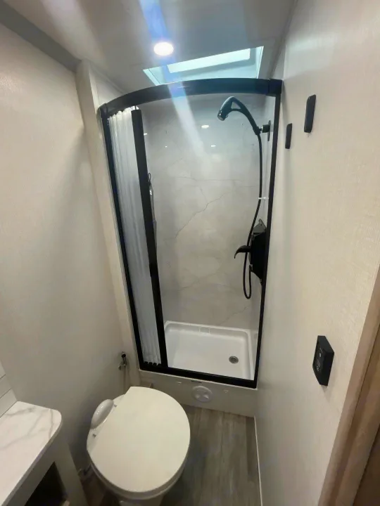 Compact RV rental bathroom featuring a modern shower with black fixtures, a white toilet with bidet, and sleek grey finishes.. Isata 3 Series 2026