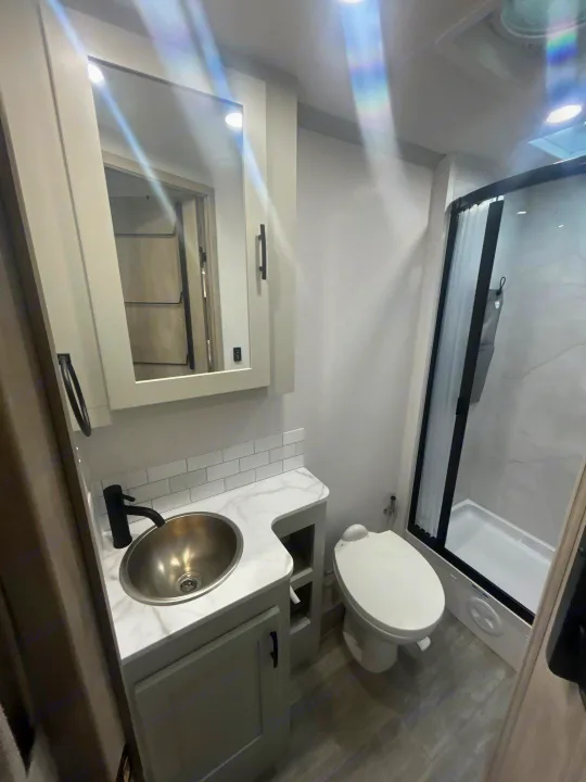 Inside an RV rental: a modern, light-filled bathroom with a gray vanity, stainless sink, toilet, and black-framed shower.. Isata 3 Series 2026
