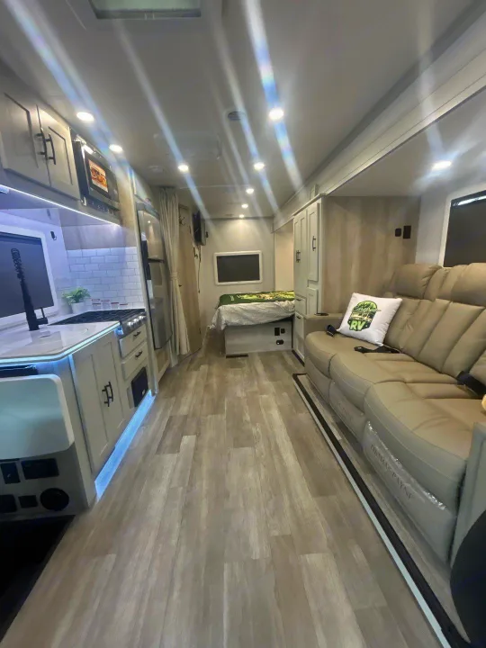 Bright, modern RV rental interior featuring a kitchen, spacious living area with sofa, and rear bed. Wood-look flooring.. Isata 3 Series 2026