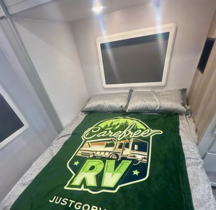 Cozy rv rental bedroom showing a bed with a green "Carefree RV" blanket and two pillows. Ideal for your next trip.. Isata 3 Series 2026