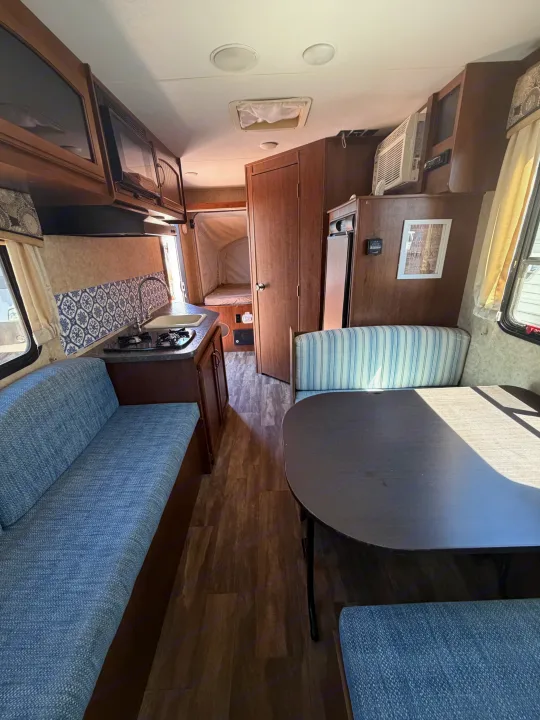 Cozy RV rental interior with a kitchen, dinette, and bed area. Features wood cabinetry, blue seating, and a compact design.. Jayco Jay Feather 2017
