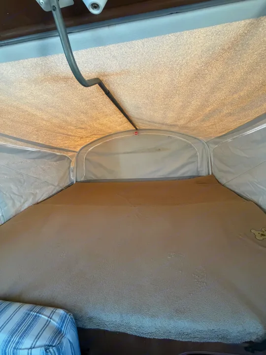 Cozy bed inside an rv rental pop-up camper, featuring fabric walls/ceiling and a soft blanket with a teddy bear.. Jayco Jay Feather 2017
