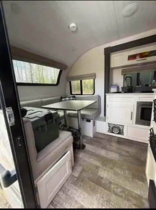 Modern rv rental interior showing a dinette, compact kitchen with microwave, and wood-look floor.. R-Pod Hood River Edition 2021