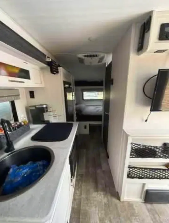 Spacious RV rental interior featuring a modern kitchenette with sink & coffee maker, living area with TV, and rear bedroom.. R-Pod Hood River Edition 2021