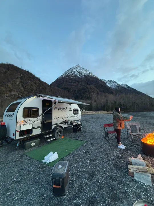Cozy rv rental camping trip: woman by campfire, R-Pod trailer, and snowy mountains at dusk.. R-Pod Hood River Edition 2021