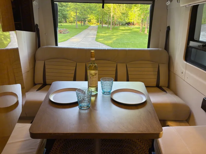 Relaxing rv rental interior: dinette with wine, glasses, plates, and a green outdoor view through the large window.. Winnebago Era 2017