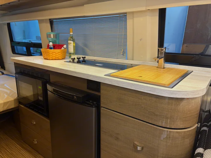 RV rental kitchen featuring a compact counter, sink, stovetop, microwave, and fridge, integrated into modern wood-look cabinetry.. Winnebago Era 2017