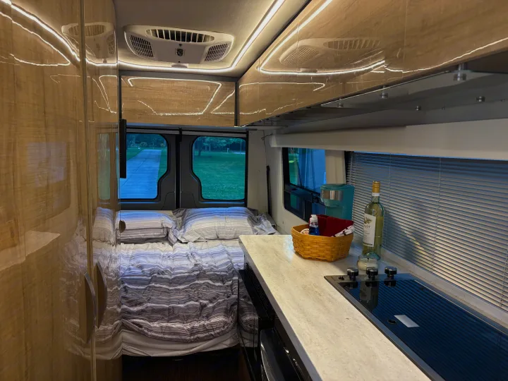 Modern rv rental interior: a comfy bed, sleek kitchen counter with stove, and warm overhead lighting. Ready for travel!. Winnebago Era 2017
