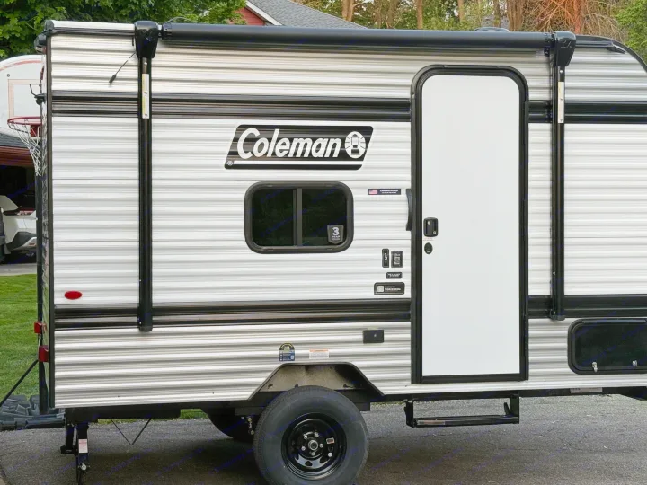 This Coleman RV rental, a striped travel trailer, features a side door, window, and retracted awning, ready for your next adventure.. Keystone RV Coleman 13B 2026