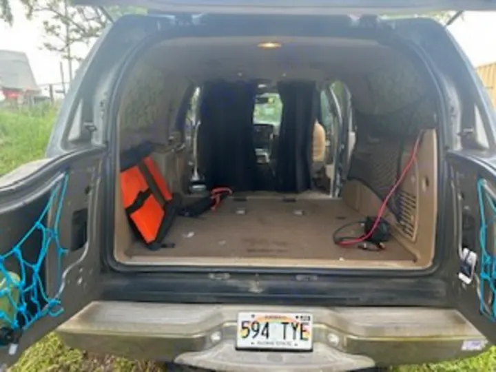DIY RV rental alternative: SUV cargo area open, converted for car camping with rear storage nets & internal privacy curtains.. Ford Excursion 2000
