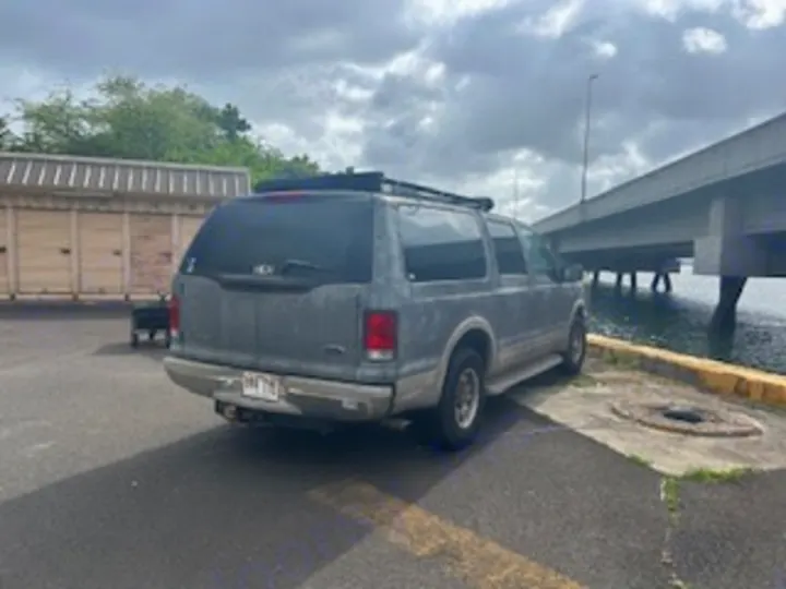 A gray Ford Excursion SUV, an ideal RV rental alternative for adventure, parked waterfront beside a bridge.. Ford Excursion 2000