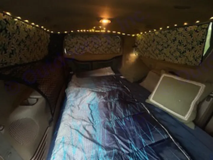 This cozy RV rental's van interior features a comfortable bed, string lights, & patterned window coverings for travel.. Ford Excursion 2000