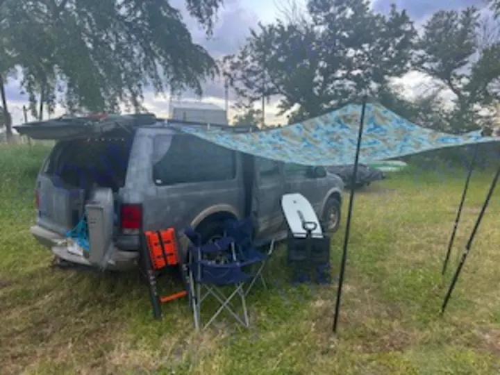 Converted van camping setup in a grassy field, offering an outdoor adventure like a compact RV rental with a tarp canopy and gear.. Ford Excursion 2000