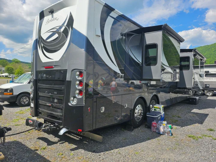 A large, black and white Berkshire XLT rv rental with extended slide-outs, packed with coolers and groceries, parked on gravel for camping.. Forest River Berkshire XLT 2024