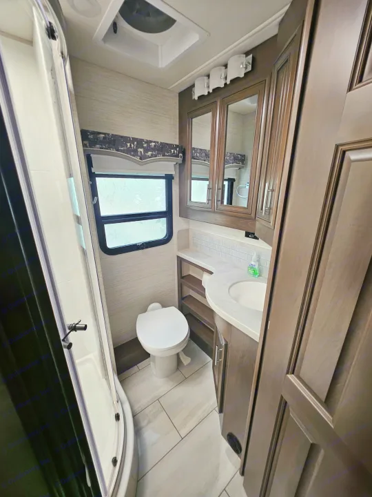 RV rental bathroom featuring shower, toilet, window, wood vanity with sink, and tiled floor.. Forest River Berkshire XLT 2024