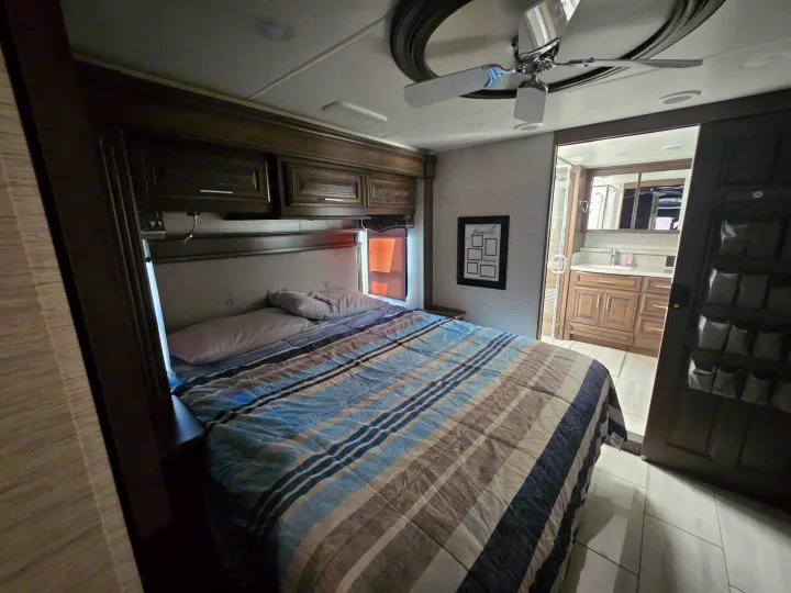 Spacious RV rental bedroom with cozy bed, overhead storage, ceiling fan, and adjacent bathroom.. Forest River Berkshire XLT 2024