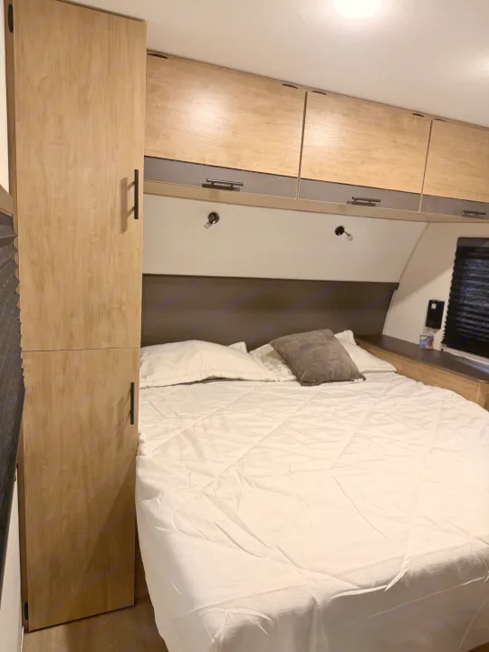 Cozy RV rental bedroom features light wood cabinets, a comfortable bed with white quilting, and reading lights above.. Forest River Campsite Reserve 2026