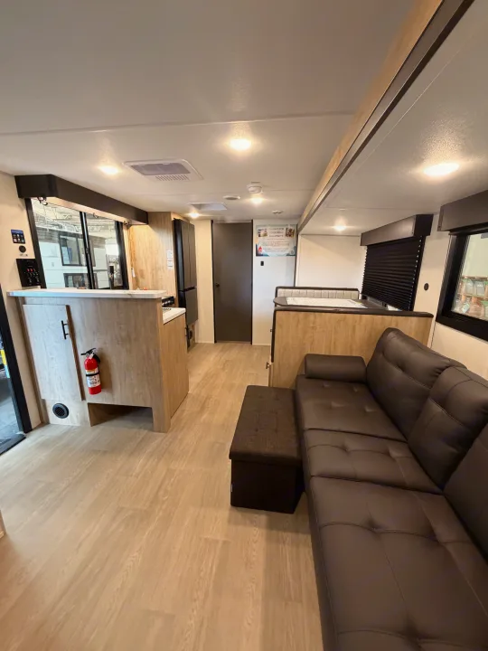 Modern rv rental interior with an L-shaped sofa, kitchenette, and dinette, featuring light wood-look flooring.. Forest River Campsite Reserve 2026