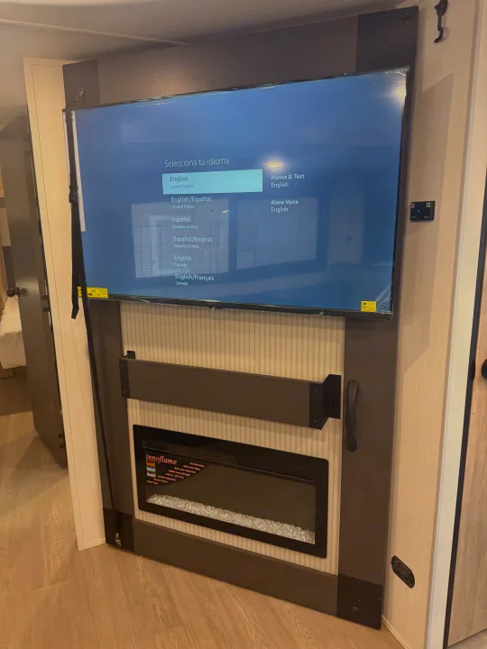 RV rental: Interior view of a TV displaying language selection over an electric Innoflame fireplace, secured for travel.. Forest River Campsite Reserve 2026