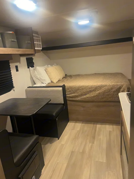 Cozy RV rental interior with a comfortable bed, dinette, overhead storage, and modern wood-look flooring.. Heartland Prowler Lynx 17BHX 2025