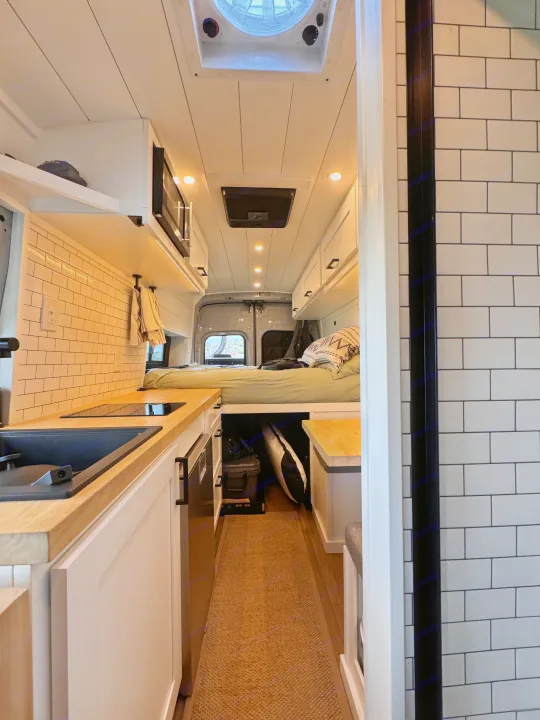 Modern camper van interior with kitchen, bed, and white subway tile backsplash, ideal for rv rental or van life.. ActiVan Ford Transit 350 AWD 2023