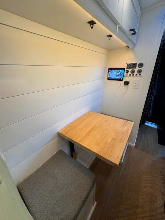 Cozy dining and control panel area in an RV rental, featuring a wooden table, gray bench, and white shiplap walls.. ActiVan Ford Transit 350 AWD 2023