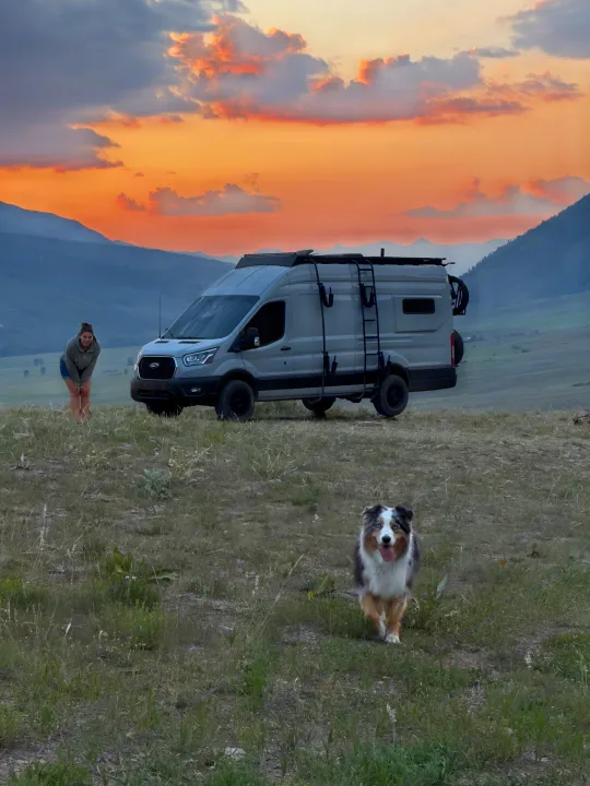 Embrace van life! An RV rental, a woman, and her happy dog at sunset in the mountains. Perfect for outdoor adventures.. ActiVan Ford Transit 350 AWD 2023