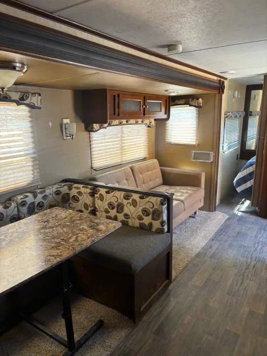 This RV rental interior offers a comfortable dinette booth, a sofa, overhead cabinets, and a glimpse of the bedroom area.. Keystone RV 28BHS 2016