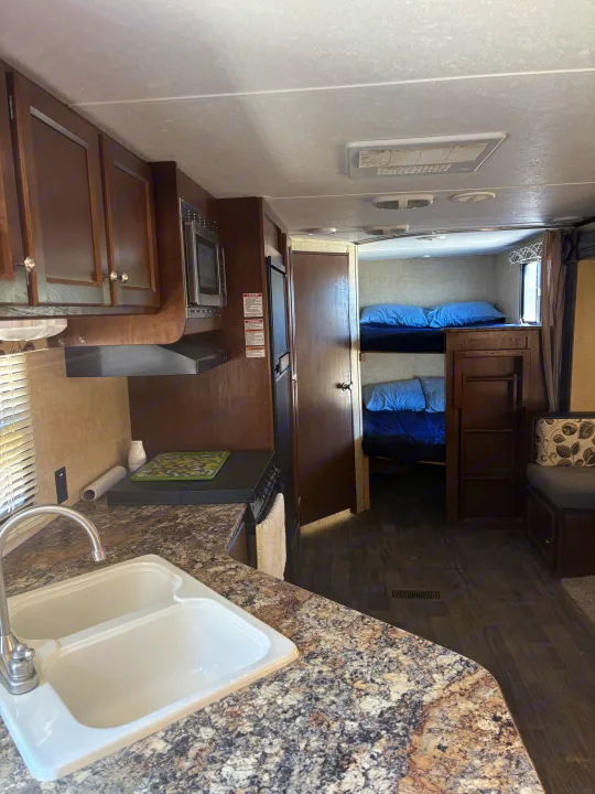 An RV rental interior featuring a practical kitchen with sink, stove, and microwave, plus cozy bunk beds.. Keystone RV 28BHS 2016