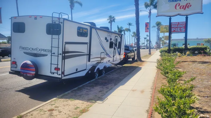 Freedom Express travel trailer, great for an RV rental, parked on a sunny street with palm trees and local businesses.. Coachmen 292bhs 2021