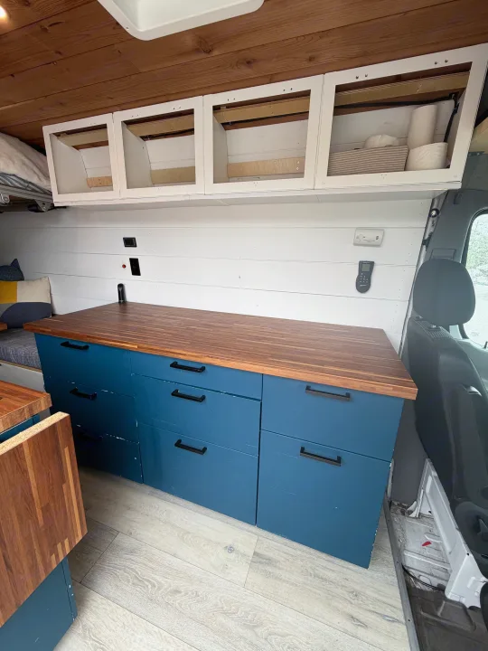 Inside an rv rental, featuring a custom campervan interior with blue storage cabinets, wood counter, and overhead compartments.. Mercedes Sprinter 2010