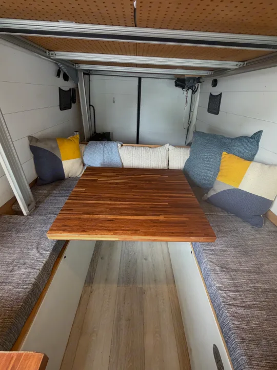 RV rental interior: A compact dining area featuring a butcher block table, cushioned benches, and colorful pillows.. Mercedes Sprinter 2010