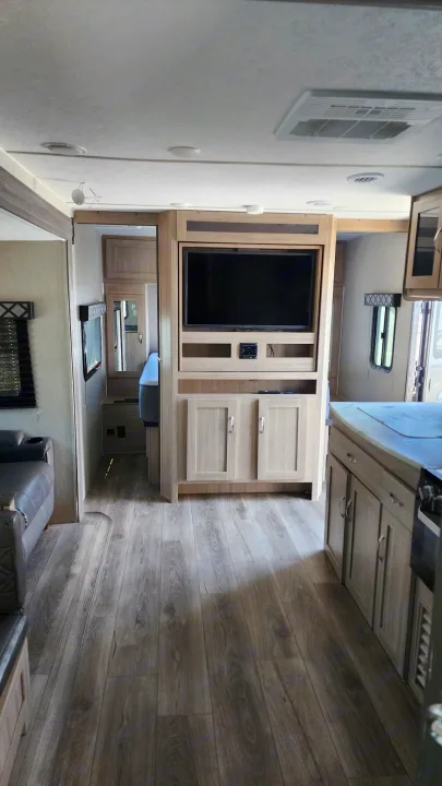 Modern RV rental interior with entertainment center, kitchen, and light wood-look flooring.. Coachmen 292bhs 2021