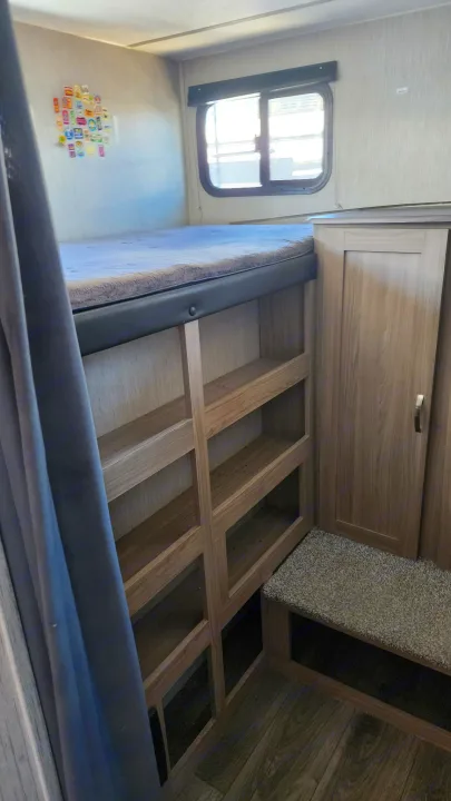 Cozy rv rental bunk beds with shelves & cabinet, offering practical storage and a window view in this camper interior.. Coachmen 292bhs 2021