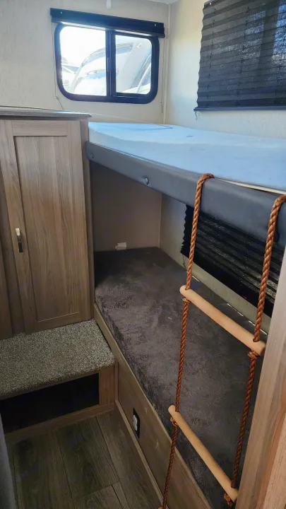This RV rental features bunk beds with a rope ladder, a window, and a wardrobe, providing comfortable sleeping and storage.. Coachmen 292bhs 2021